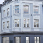 Mehrgeschossiges Gebaeude an einer Strassenecke mit mehreren Fenstern.